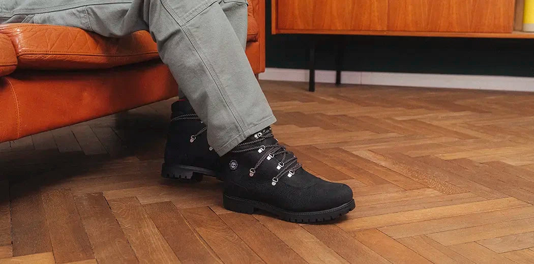 A person wearing Timberland black boots sitting on a wooden floor.