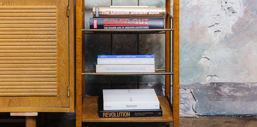 A book on a shelf by a window, surrounded by magazines for women.