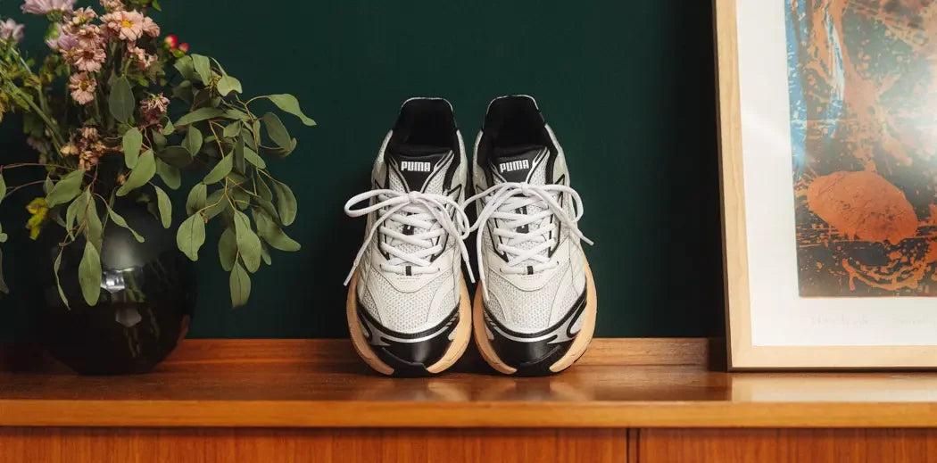  A pair of Puma Velophasis sneakers on a shelf, placed next to a framed picture.