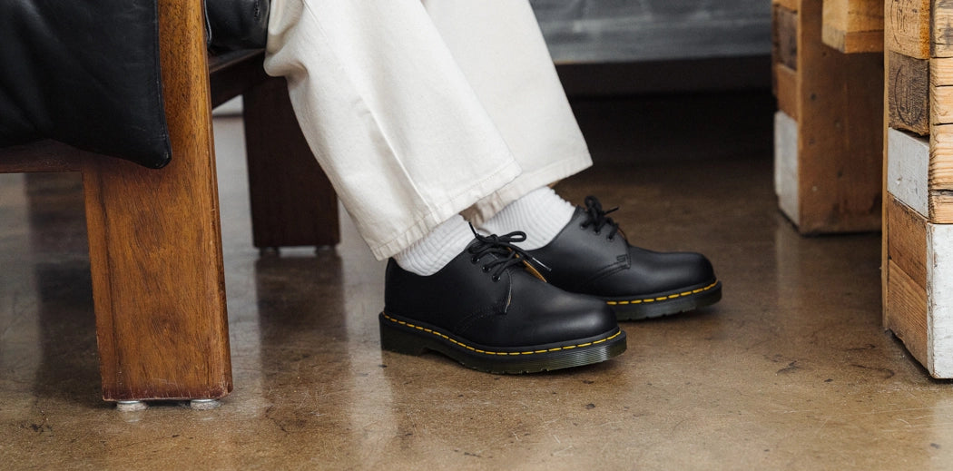  A pair of black leather Dr. Martens boots with yellow stitching and a thick sole.