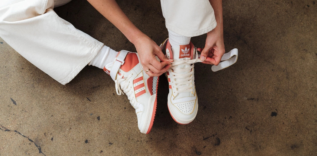 A person holding a pair of adidas Forum sneakers.