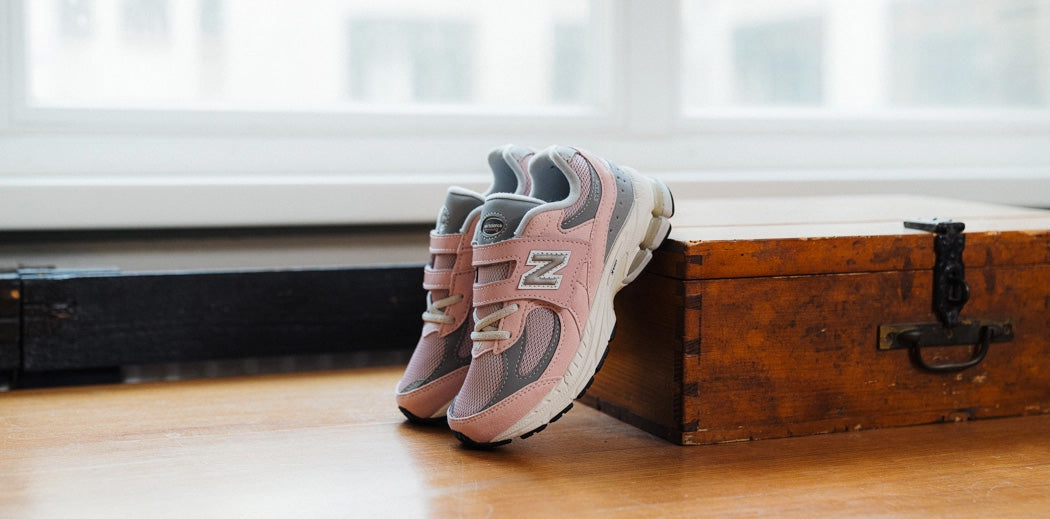 Pink and grey sneakers for pre school kids resting on a wooden table.